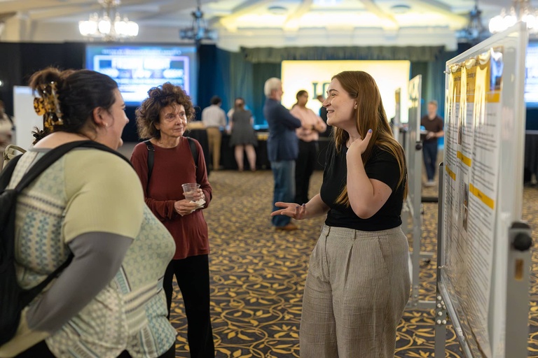 A graduate student presents their research to two visitors at the 2025 Jakobsen Conference.